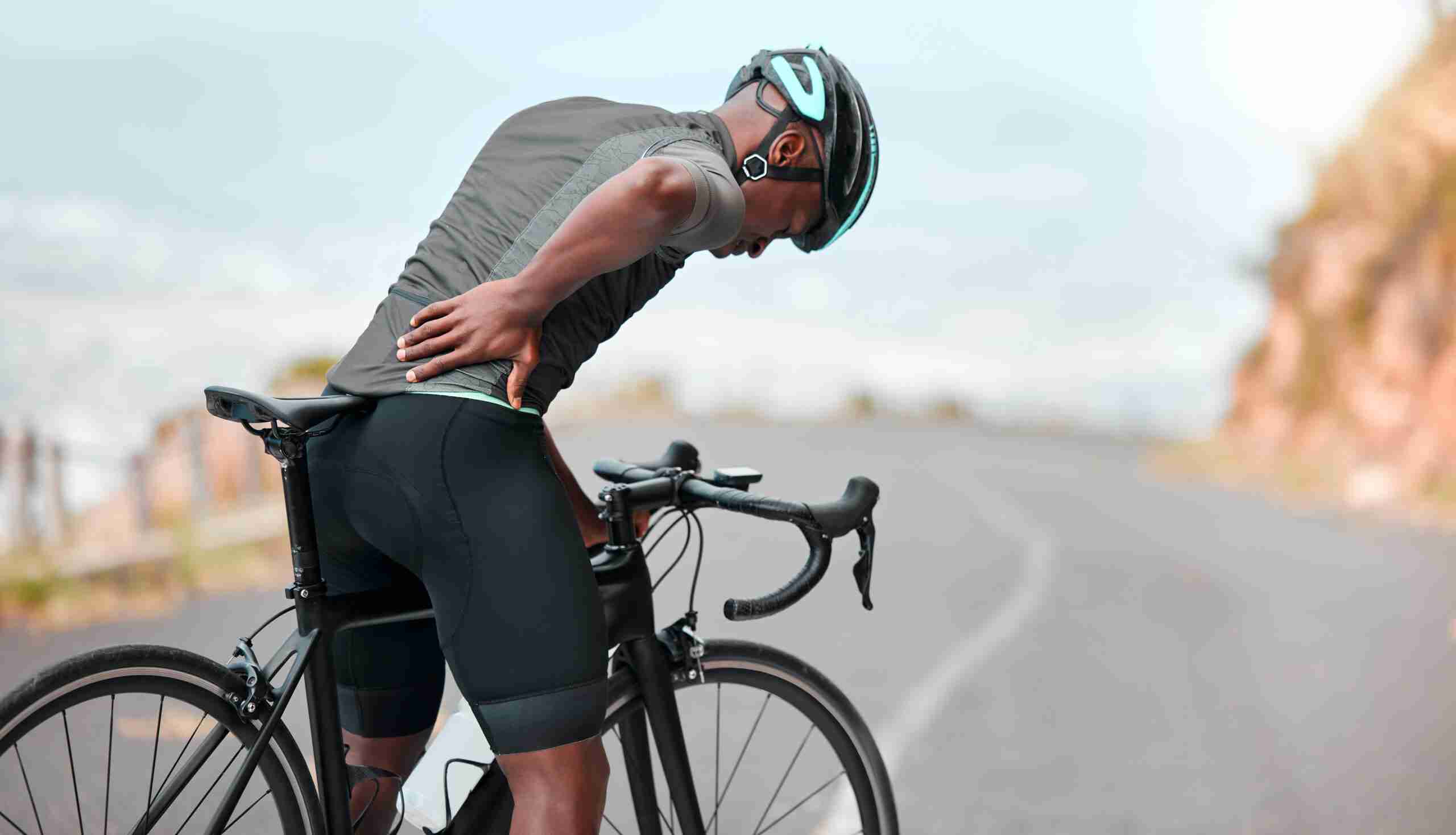 Fitness, sports injury and back pain by man cyclist feel uncomfortable while cycling along mountain route. Training, pain and injured athletic guy suffering from joint, muscle and spinal discomfort man on bike in need of sports and injury rehabilitation