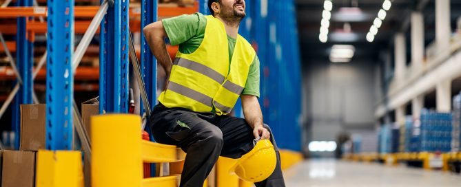 A warehouse worker having back pain and rubbing it.