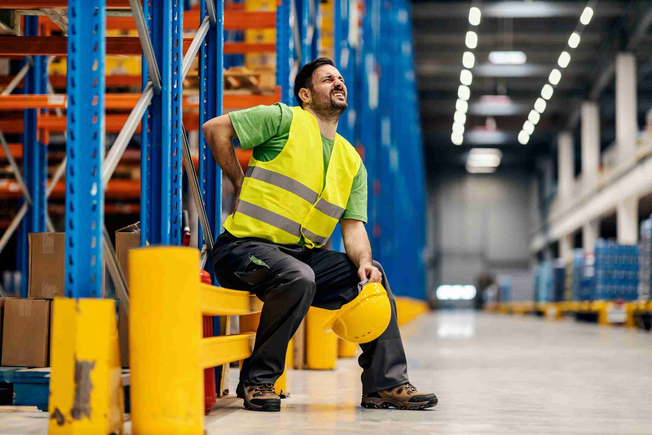 A warehouse worker having back pain and rubbing it. A warehouse worker having back pain and rubbing it.